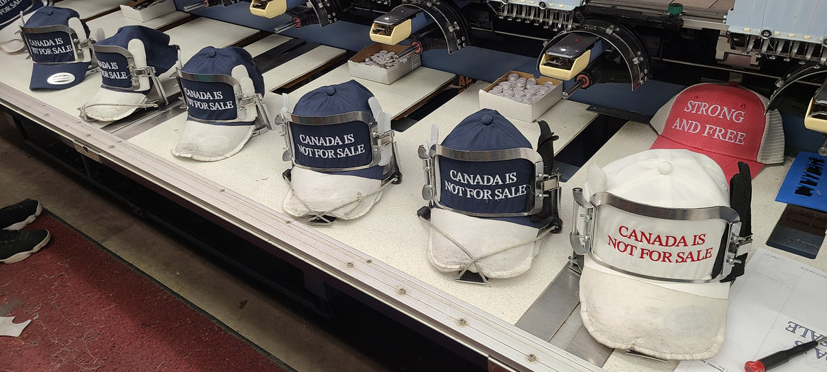 Canada is Not For Sale hats lined up at embroidery machines